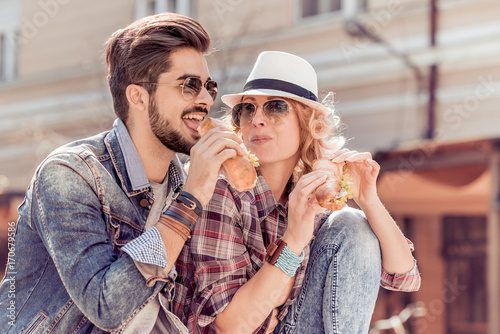 Couple eating sandwich and talking outdoor.