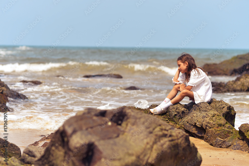 Little girl sitting on rocky seashore