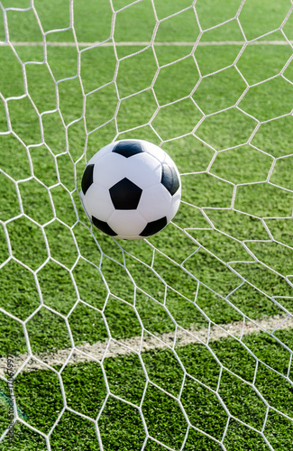 Soccer football in Goal net with green grass field.