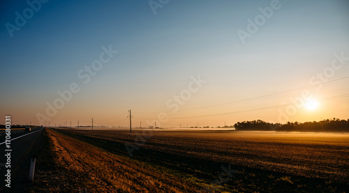 Panoramic view of sunrise over fields farming in fog and asphalt road