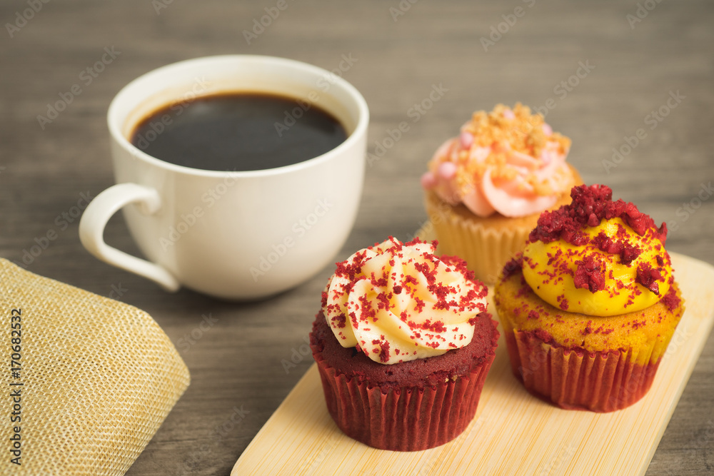Black coffee cup with red velvet and strawberry cupcakes on wooden plate on wooden table top Black coffee cup with red velvet and strawberry cupcakes on wooden plate on wooden table top