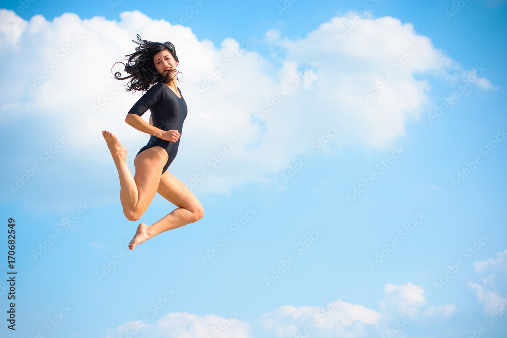 A young woman in tights is engaged in gymnastics and jumps, drains, leads herself into a good shape. Pleasure from training. Girl jumping against the sky A young woman in tights is engaged in gymnastics and jumps, drains, leads herself into a good shape. Pleasure from training. Girl jumping against the sky