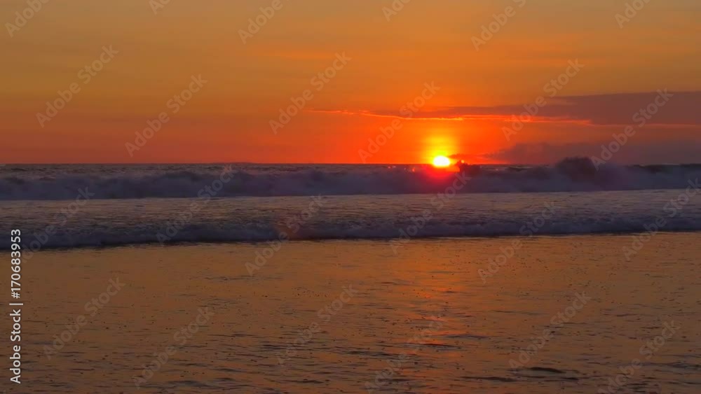 Surf break waves breaking and rolling towards the sea shore at bonfire-red sunset on tranquil summer evening in dreamy Bali island, Indonesia. Deep blue rippling sea splashing at golden light sunset Surf break waves breaking and rolling towards the sea shore at bonfire-red sunset on tranquil summer evening in dreamy Bali island, Indonesia. Deep blue rippling sea splashing at golden light sunset