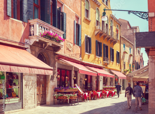 Fototapeta Naklejka Na Ścianę i Meble -  Colorful cozy street with tables of cafe at  a sunny morning, Venice, Italy.    Toned image