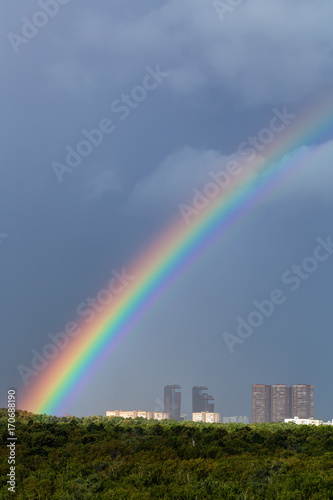 rainbow in rain over city and green trees