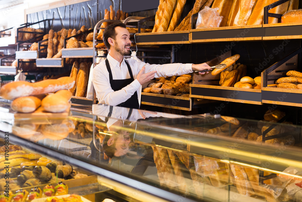 Male shop assistant demonstrating delicious loaves of bread in bakery