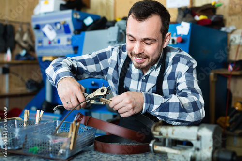 Male worker making hole in belt in specialized workshop