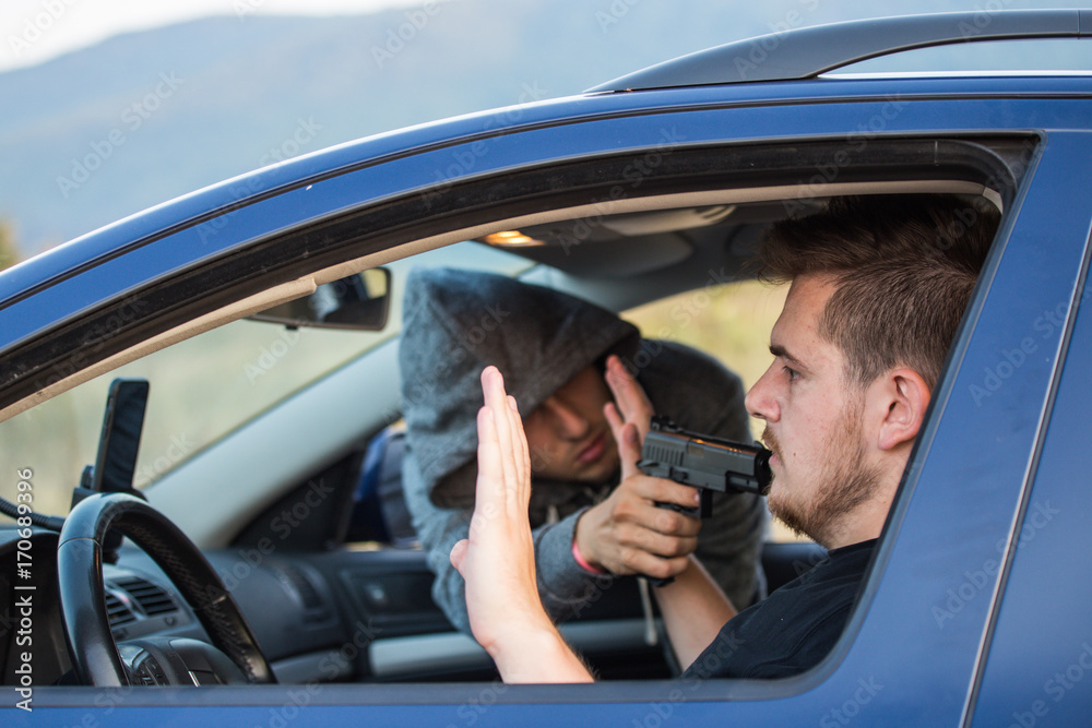 A thief, a criminal with a pistol threat, tries to steal a car, sits at the passenger's seat and holds a pointed gun in the driver's car A thief, a criminal with a pistol threat, tries to steal a car, sits at the passenger's seat and holds a pointed gun in the driver's car