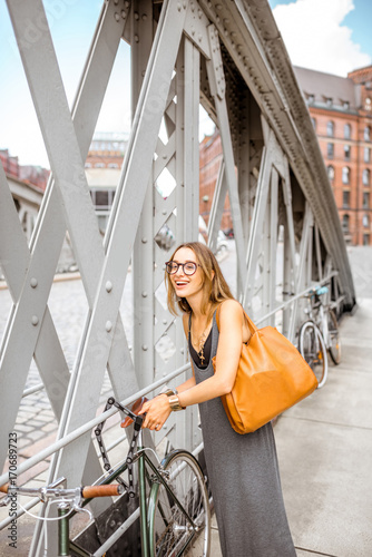 Young stylish business woman parking retro bicycle on the iron bridge
