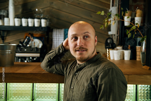 Young serious fashionable man sitting alone at the bar counter in loft-styled cafe. Former factory building, natural daylight.