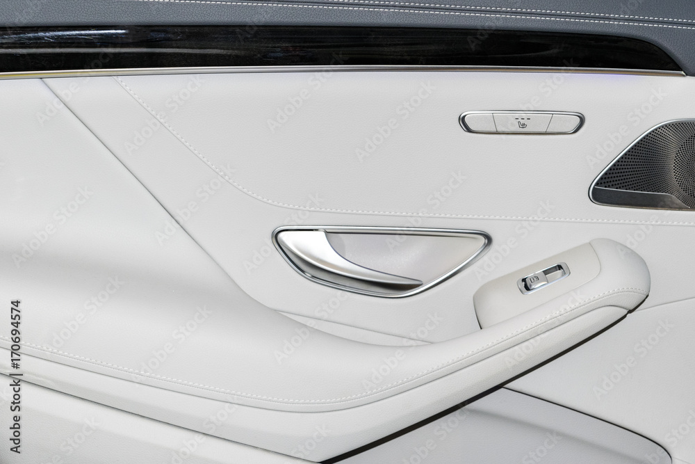 Door handle with Power seat and window control buttons of a luxury passenger car. White leather interior of the luxury modern car. Modern car interior details