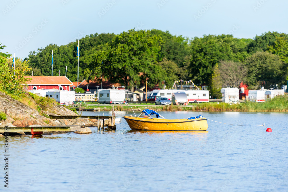 One open yellow motorboat moored to a pier with camping site in background. Location Karlskrona, Sweden.