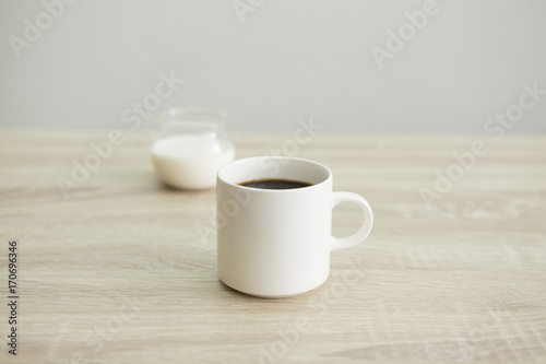 WHITE COFFEE CUP WITH MILK JAR White coffee cup with transparent milk jar on the wood table. 