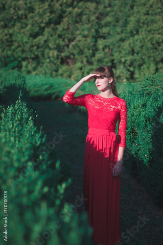 Beautiful young girl in a long red dress in an autumn park. photo