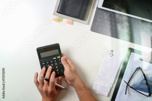 top view of businessman hand working with finances about cost and calculator and latop with mobile phone on withe desk in modern office