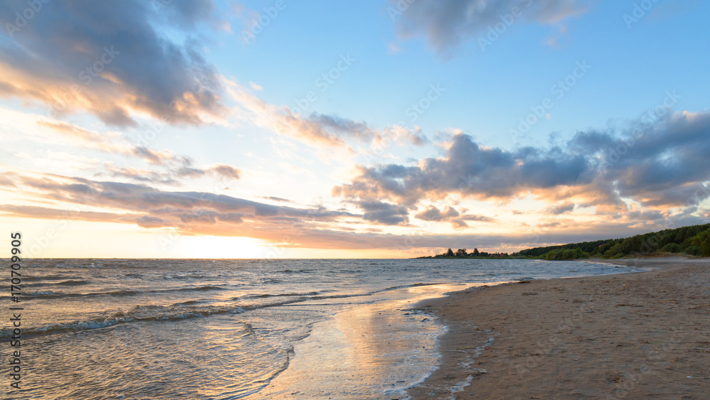 Fototapeta premium Quiet empty beach at sunset on a background of blue sky with clouds