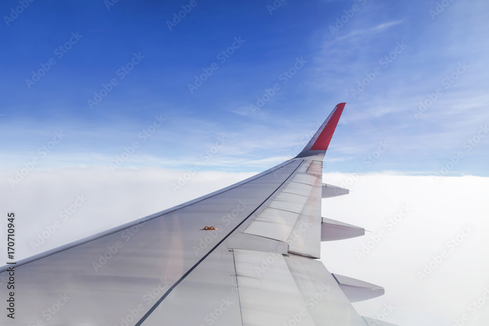 Wing of commercial airplane view from right the window of the plane flying above the clouds on blue sky in clear day