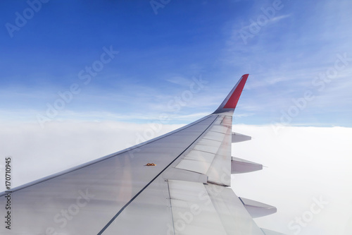 Wing of commercial airplane view from right the window of the plane flying above the clouds on blue sky in clear day