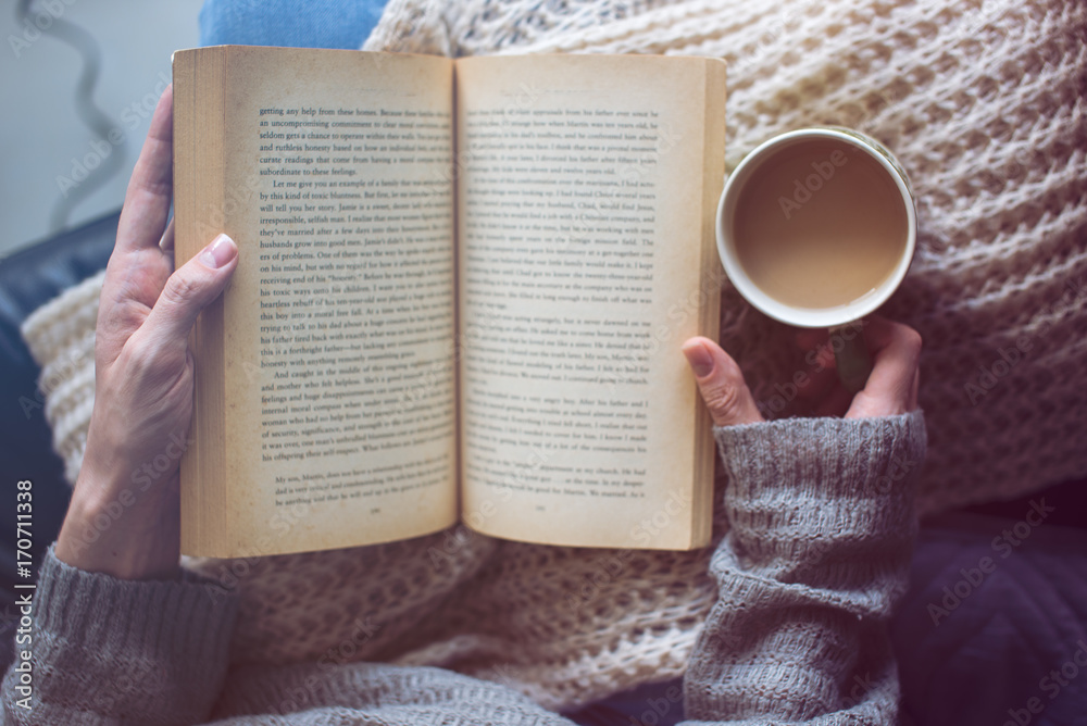a woman is reading a book and holding coffee - obrazy, fototapety, plakaty 