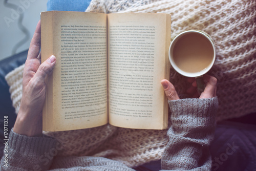 a woman is reading a book and holding coffee photo