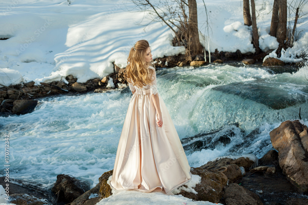 Beautiful young girl in a chic dress in the nature next to the river