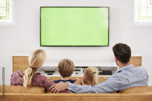 Fotografi Rear View Of Family Sitting On Sofa In Lounge Watching Television