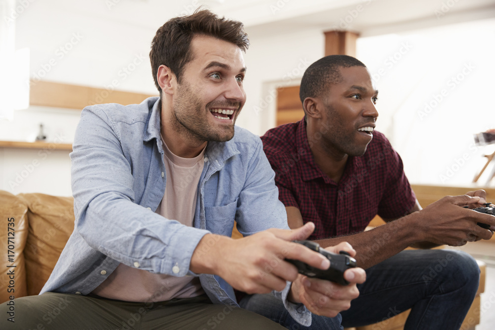 Two Male Friends Sitting On Sofa In Lounge Playing Video Game Two Male Friends Sitting On Sofa In Lounge Playing Video Game