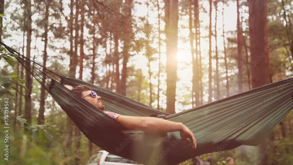 A young man relaxes on a hammock in the forest.