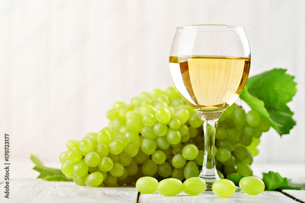 A glass of white wine and fresh grapes on a wooden table. A glass of white wine and fresh grapes on a wooden table.