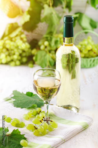 A glass of white wine, fresh grapes and a bottle of white wine on a wooden table.