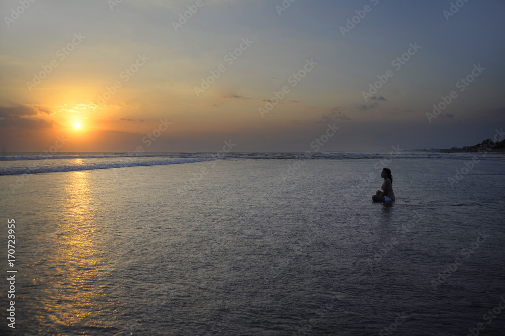 Silhouette of young beautiful asian woman sitting on sand water free and relaxed looking at the sun on sunset beach