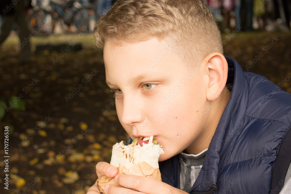 the boy with white hair in a blue vest eats a burrito the boy with white hair in a blue vest eats a burrito