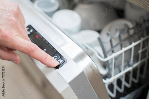 Close Up Of Woman’s Hand Pressing Start Button On Dishwasher