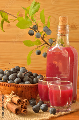 Bottle of sloe gin and filled wine glasses among a sloe berries and cinnamon bark
