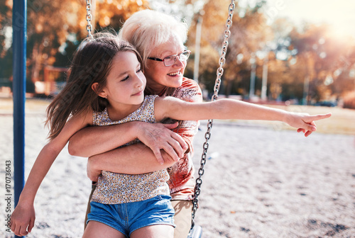 Obraz na plátně Cute little girl and her grandmother having fun on the playground in the park