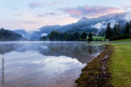 Alpine mountain summer lake at cloudy foggy sunrise