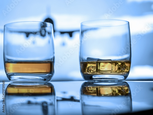 Whiskey neat and on ice close up view on reflective surface at the airport with airplane in the air.