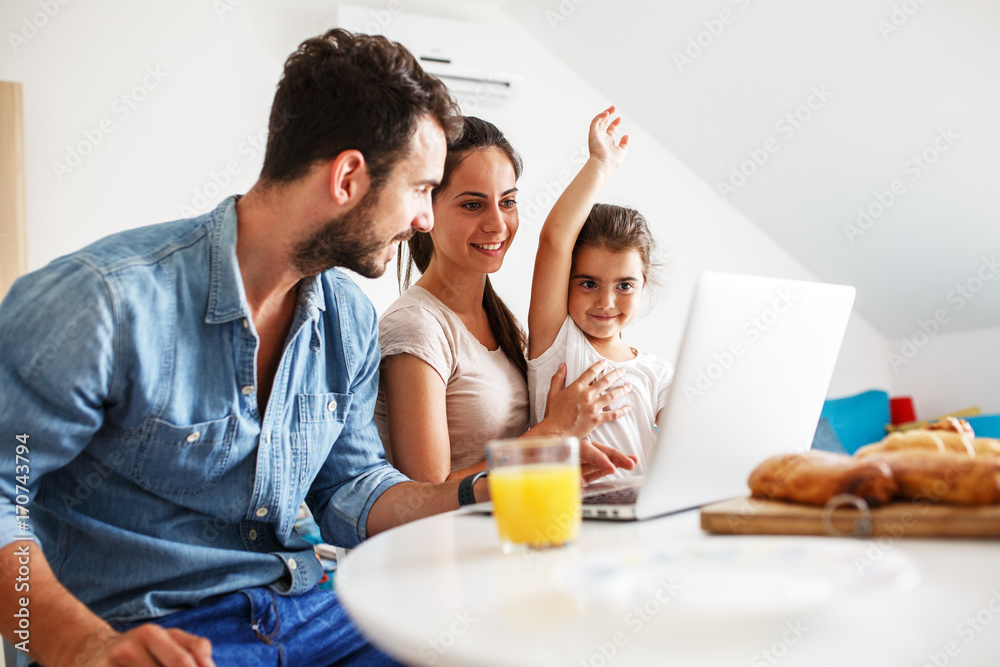 Family breakfast.Young parents with they daughter sitting at the table and watching something on laptop.