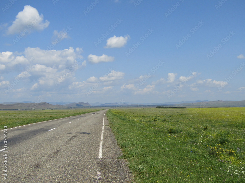 Asphalt road through the meadows on the background of sky with clouds