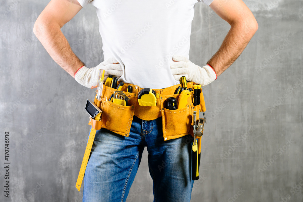unknown handyman with hands on waist and tool belt with construction tools against grey background. DIY tools and manual work concept unknown handyman with hands on waist and tool belt with construction tools against grey background. DIY tools and manual work concept