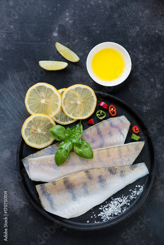 Metal plate with fresh uncooked sudak fillet, lemon, sea salt and olive oil. Flat-lay, vertical shot