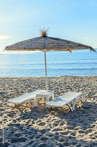 Straw sun umbrellas and white plastic sunbeds  beach with sand near blue sea water