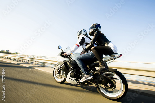 Young couple wearing leather jackets and stylish sunglasses riding on motorcycle