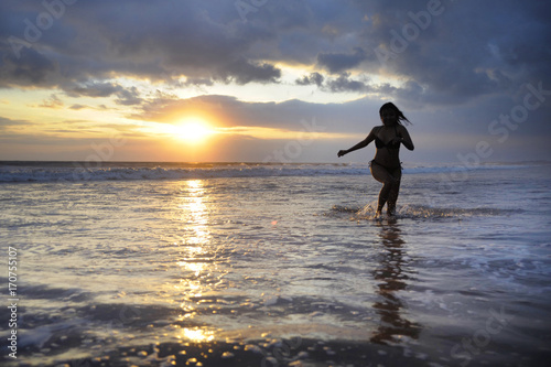 Silhouette of young beautiful and sexy asian woman running free and happy having fun at sunset beach in Bali