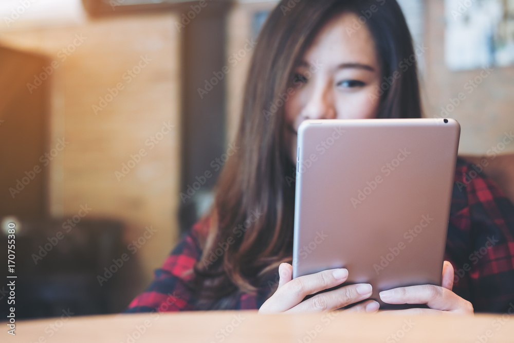 Closeup image of a smiley beautiful Asian woman holding ,using and looking at tablet pc sitting in modern cafe Closeup image of a smiley beautiful Asian woman holding ,using and looking at tablet pc sitting in modern cafe