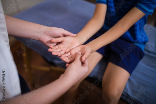 Midsection of female therapist examining hands with boy sitting