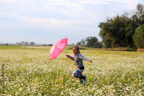 Śliczna dziewczynka biega z parasolką wśród polnych kwiatów.