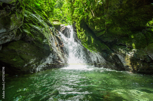 Beautiful small waterfall located inside of a green forest with stones in river at Mindo