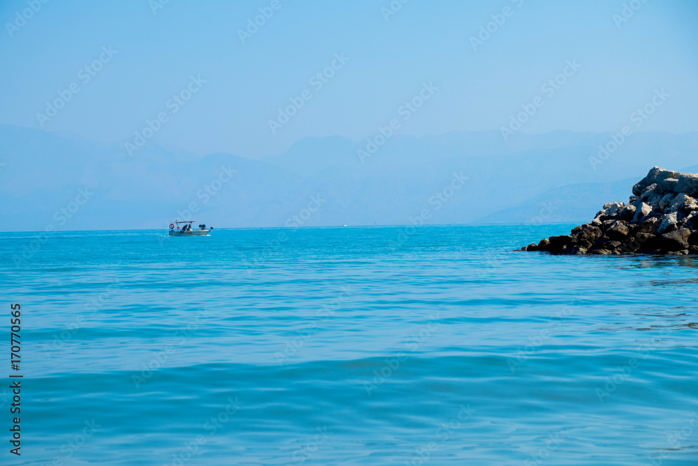 Fototapeta premium turquoise sea with dark rocks against the blue sky with a small white boat in the background