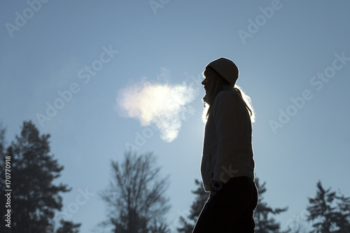 Silhouette of a woman with hat breathing warm air during a cold winter morning. Selective focus used.